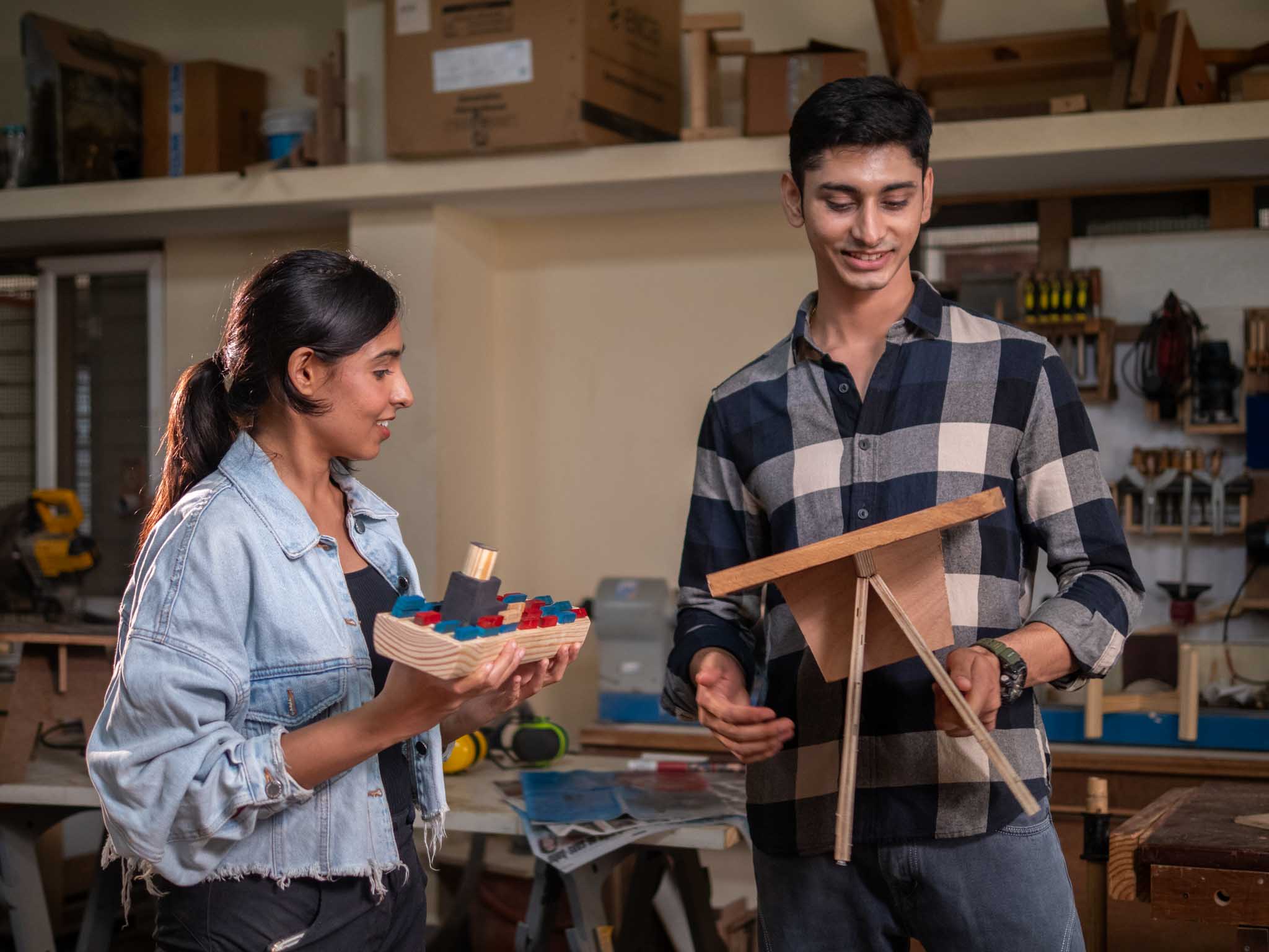 Young couple happily showing their completed wooden projects in a workshop.